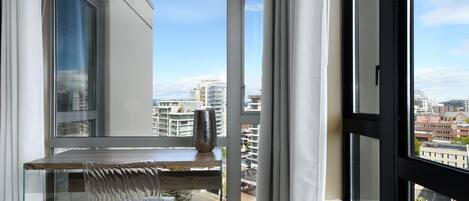 Un balcón con mesa y silla de vidrio, un jarrón decorativo y vistas de edificios de la ciudad.
