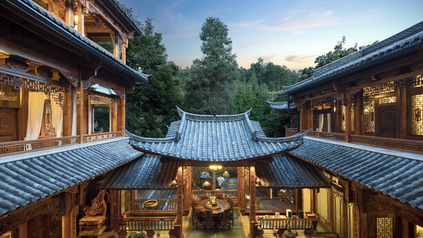 A traditional courtyard with a central wooden table and chairs, surrounded by ornate buildings with tiled roofs. - GRAND JOLI (Lijiang)