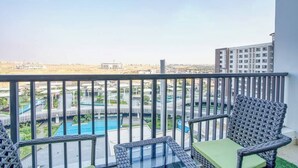 Un balcon meublé avec des meubles en osier, donnant sur une piscine et offrant une vue sur la ville.