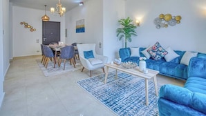 A modern living room with a blue sofa, a dining table with chairs, and a chandelier.