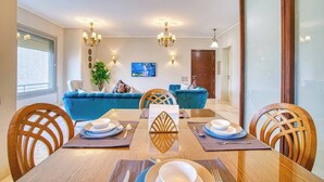 A dining area with a wooden table set for four, blue upholstered sofas, and a chandelier. - The Suite, Palm Hills - VG924, Residential Suites near AUC by ELEGANT (New Cairo City)