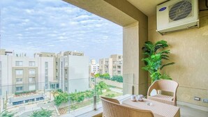 A balcony with wicker furniture, a view of the cityscape, and an air conditioning unit. - The Suite, Palm Hills - VG924, Residential Suites near AUC by ELEGANT (New Cairo City)