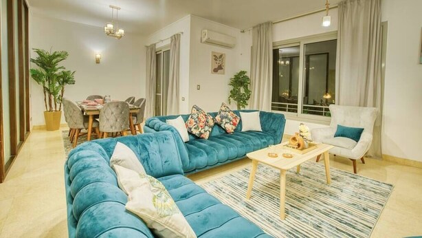 A living room with a blue sofa, a coffee table, and a dining area with chairs and a table.