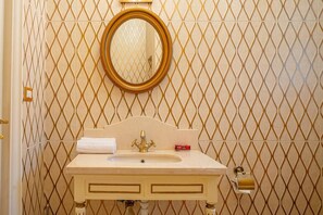 A bathroom with a diamond-patterned wall, a round mirror, a sink with a gold faucet, and a toilet with a gold lock. - The Suite, Palm Hills - V1811, Residential Suites near AUC by ELEGANT (New Cairo City)