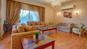 A spacious living room with a large sofa set, a glass coffee table, and a chandelier. - The Suite, Palm Hills - V1811, Residential Suites near AUC by ELEGANT (New Cairo City)