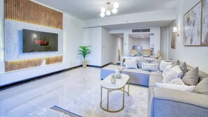A modern living room with a flat-screen TV mounted on a wooden panel, a sofa set, a coffee table, and a potted plant. - The Lofts across AUC - D108, LOFTS BY ELEGANT - WITH POOL (New Cairo City)