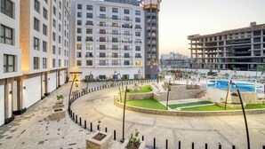 A modern hotel courtyard with a central pool, surrounded by multi-story buildings. - The Lofts across AUC - D108, LOFTS BY ELEGANT - WITH POOL (New Cairo City)