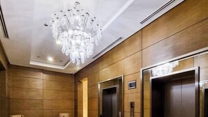 A modern lobby with a marble floor, wooden paneling, and a large chandelier. - The Lofts across AUC - D108, LOFTS BY ELEGANT - WITH POOL (New Cairo City)