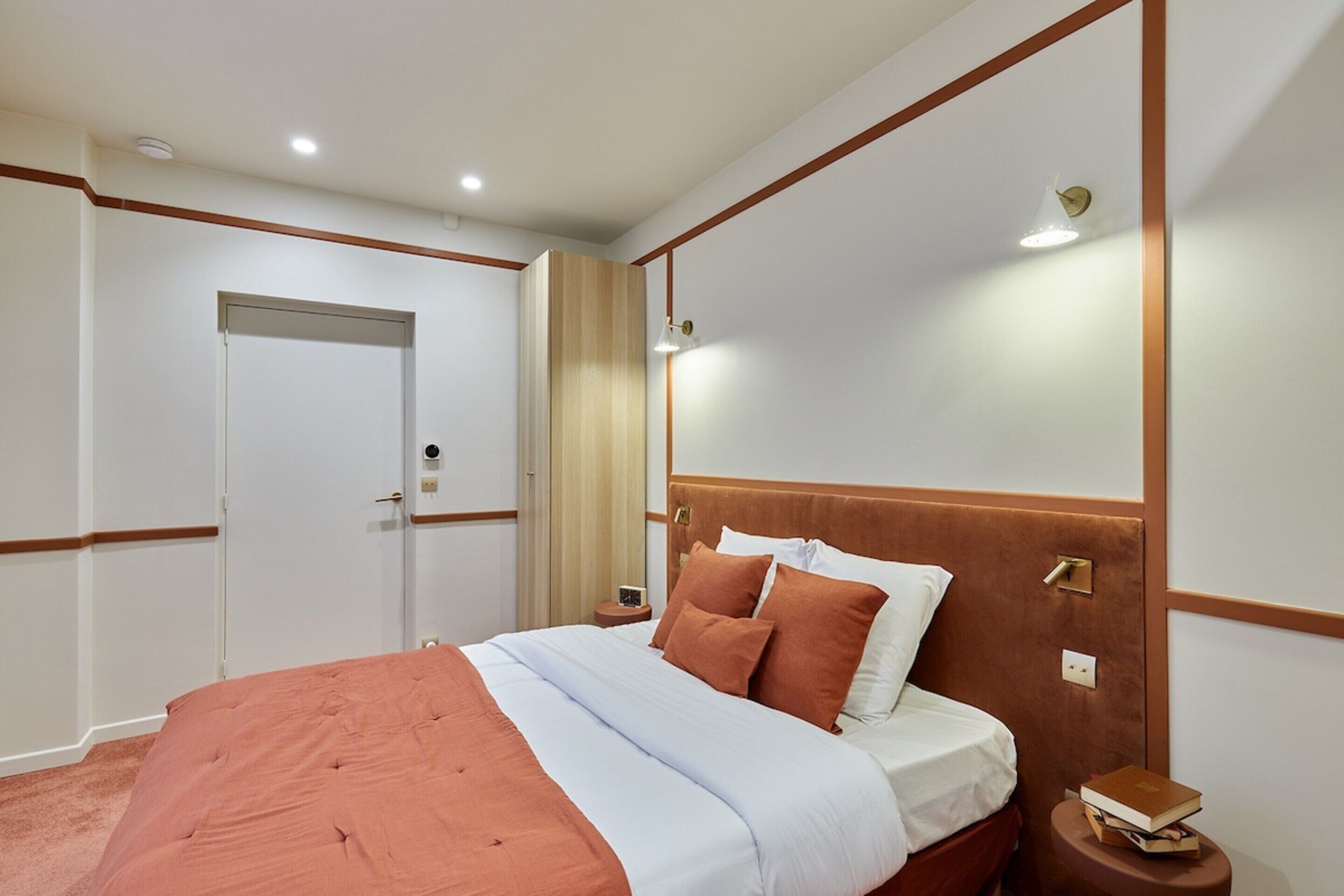 A hotel room with a bed, bedside table, and a door.
