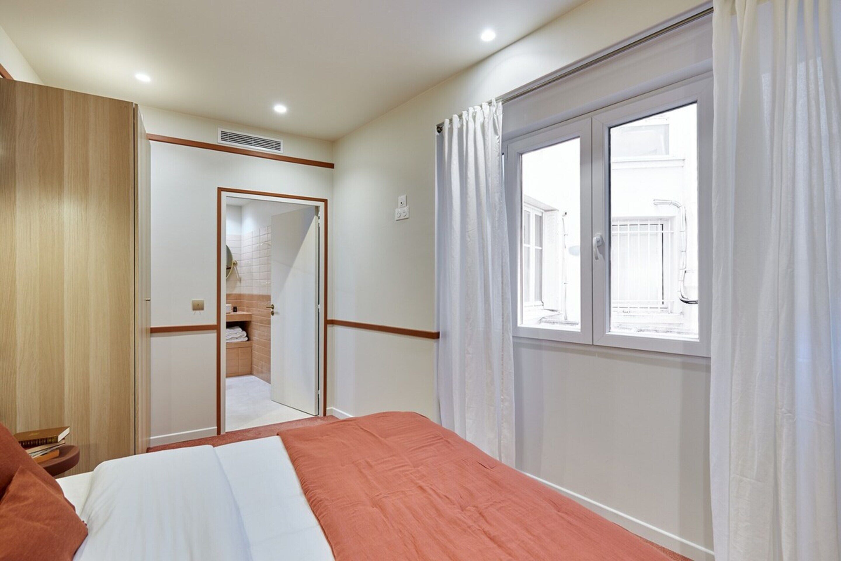 A bedroom with a bed, a wardrobe, a mirror, and a window with curtains.