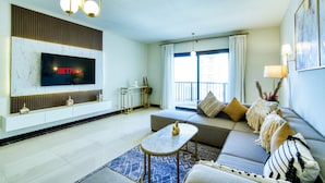 Un salon moderne avec un téléviseur à écran plat fixé sur un mur en marbre, un ensemble de canapés, une table basse et une grande fenêtre avec des rideaux.