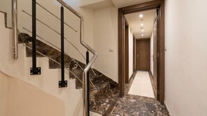 Un escalier avec des rampes en métal et des marches en marbre menant à un couloir où se trouve une porte en bois au bout.