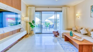 Una sala de estar moderna con televisor de pantalla plana, un sofá, una mesa de centro y un balcón con mobiliario exterior.