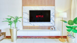 Un salón moderno con un televisor de pantalla plana montado en una pared de mármol, una consola blanca y dos plantas en macetas.