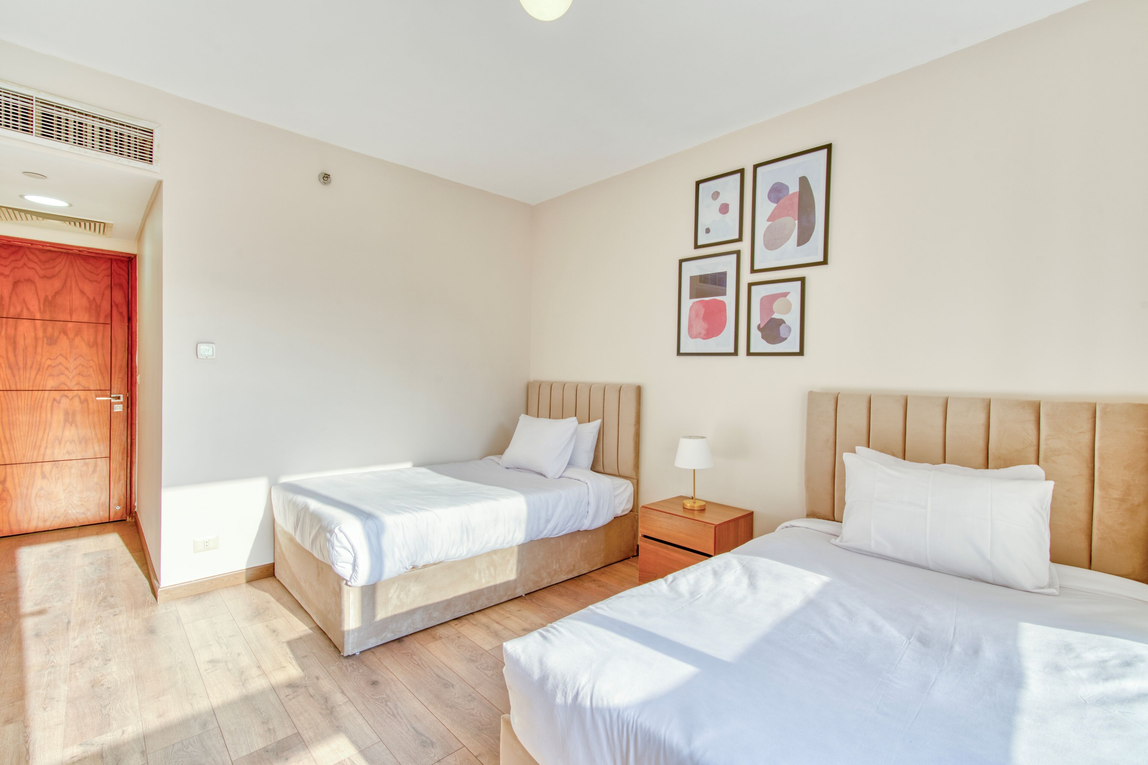 Ein Hotelzimmer mit zwei Betten, einem Holzschrank, einem Nachttisch mit Lampe und Wandbildern.