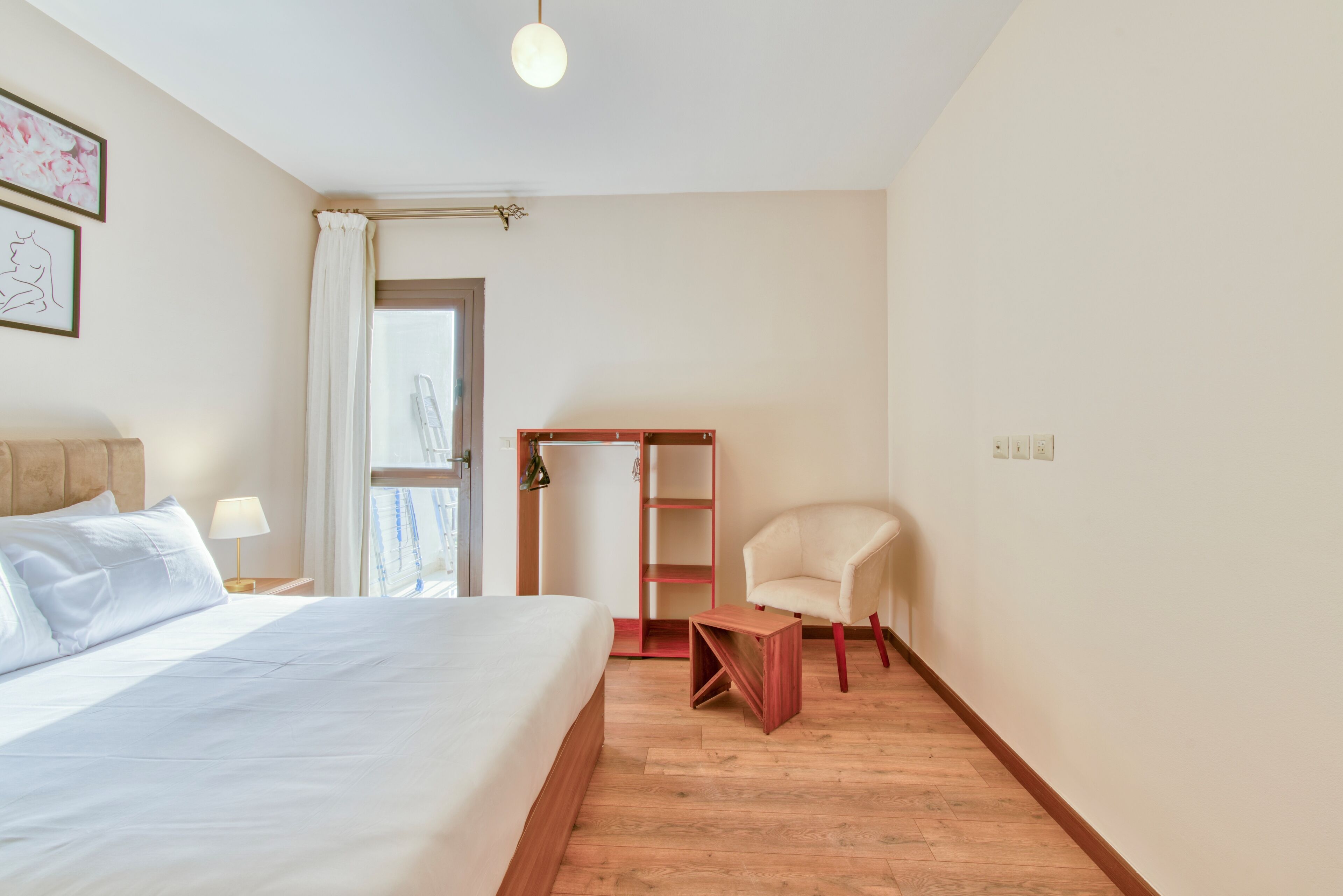 A hotel room with a bed, a chair, a small table, a wardrobe, and a window with curtains.