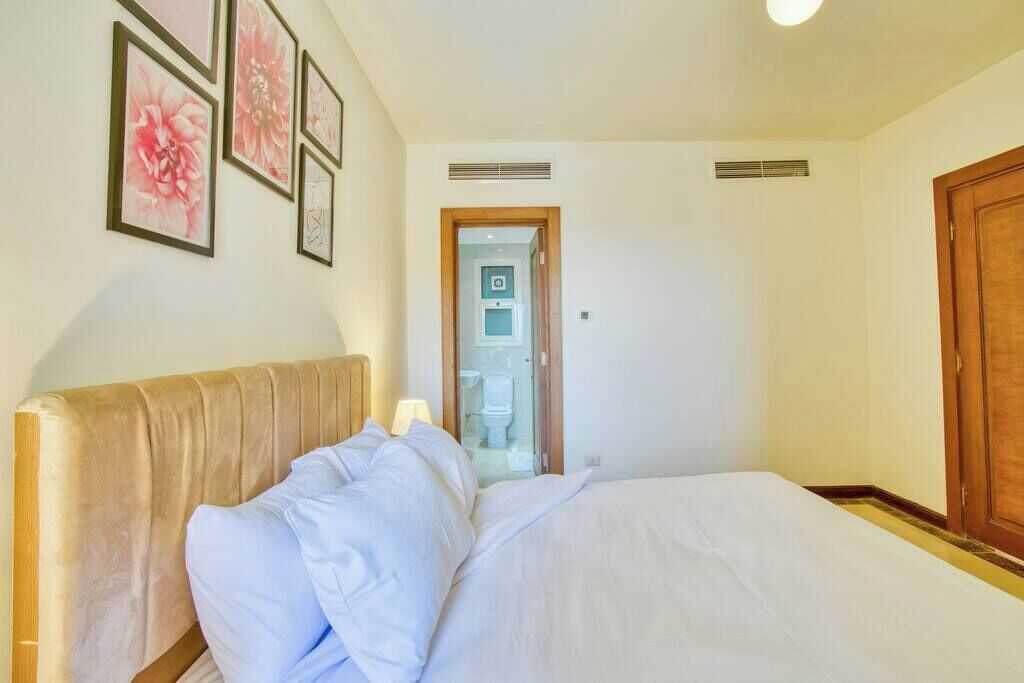 A bedroom with a bed, a wooden headboard, a door, and a bathroom visible through an open door.