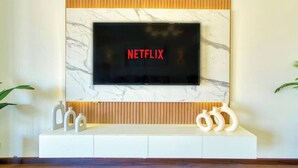A modern living room with a flat-screen TV mounted on a marble wall, a white entertainment unit below, and a wooden panel above.
