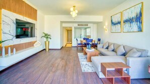 A modern living room with a flat-screen TV, a sofa, a coffee table, and a dining area with chairs and a table.