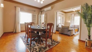 A dining area with a round table and chairs, a chandelier, and a large plant.