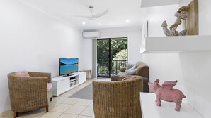 A modern living room with a television, wicker furniture, and a pink pig sculpture. - Periwinkle - Ideal Beachfront Retreat Near Main Street with Ceiling Fans, Wi-Fi & Air Con (Sawtell)