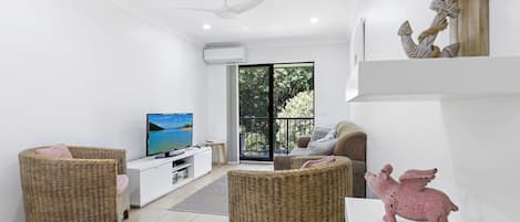 A modern living room with a television, wicker furniture, and a pink pig sculpture.