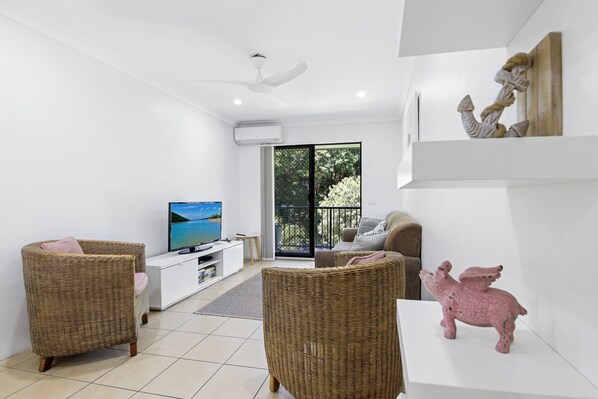 Un salon moderne avec un téléviseur, des meubles en osier et une sculpture de cochon rose.