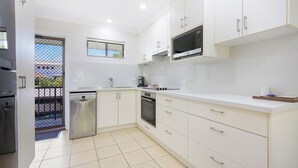A modern kitchen with white cabinets, stainless steel appliances, and a tiled floor. - Periwinkle - Ideal Beachfront Retreat Near Main Street with Ceiling Fans, Wi-Fi & Air Con (Sawtell)