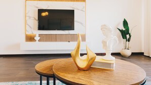 Una sala de estar moderna con chimenea de mármol, televisor de pantalla plana, mesa de centro de madera, una escultura y una planta en maceta.