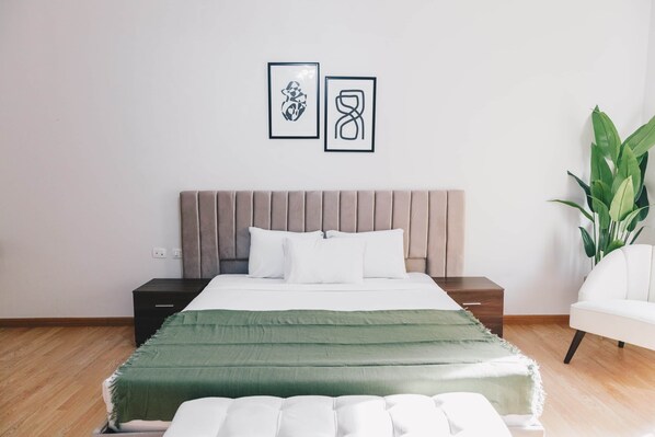 A modern bedroom with a bed, nightstands, a green throw blanket, and two framed artworks on the wall.