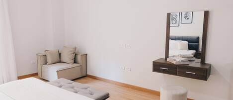 A bedroom with a bed, a bedside table, a chair, a small stool, and a wall-mounted cabinet with a mirror and framed pictures.