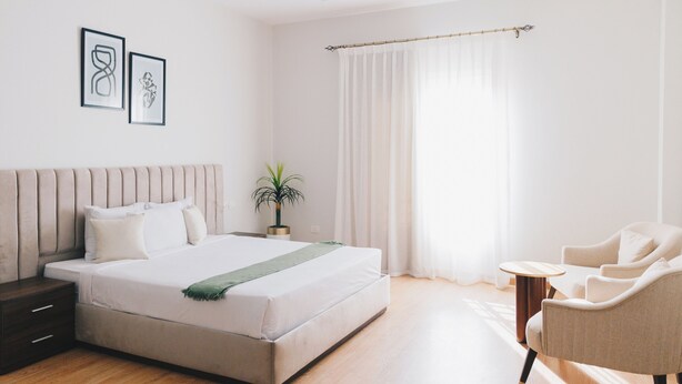 A modern bedroom with a large bed, bedside tables, a chair, and a potted plant.