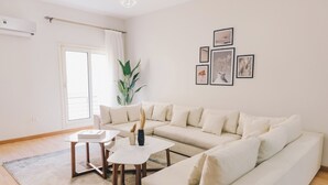 A modern living room with a beige sofa, two white coffee tables, and a large potted plant.