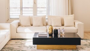 A modern living room with a white sofa, a black coffee table, and a view of a balcony through large windows. - The Seven Six Near Waterway 5A - 3, THE SEVEN SIX near WATERWAY 5A MALL By ELEGANT (New Cairo City)