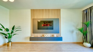 A modern living room with a flat-screen TV mounted on a wooden panel wall, a built-in entertainment unit below, and two potted plants on either side.