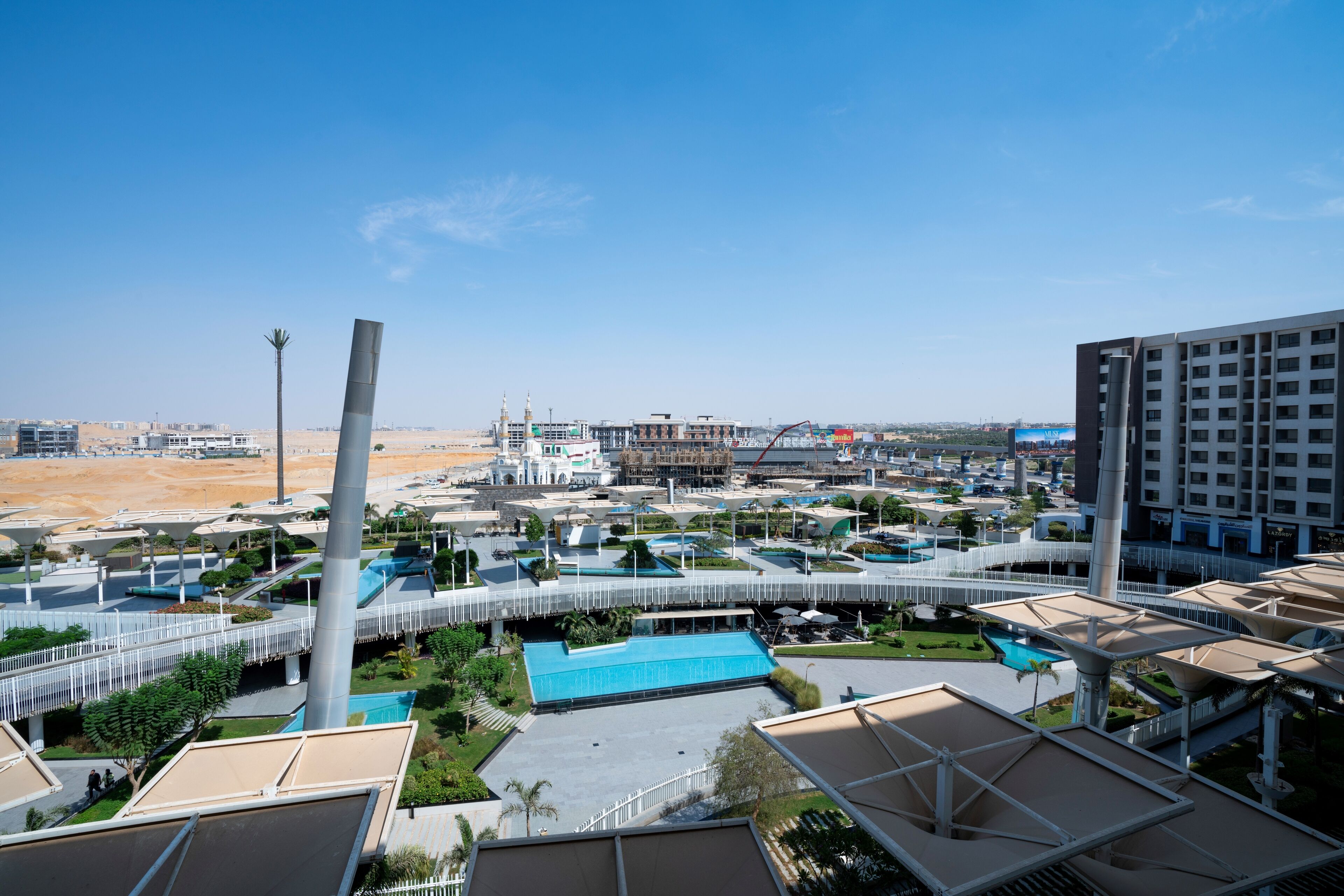 A modern hotel complex with multiple buildings, a central courtyard with a pool, and a desert landscape in the background.
