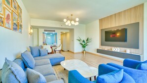 A modern living room with a sectional sofa, blue armchairs, a coffee table, and a flat-screen TV mounted on a wooden panel wall.
