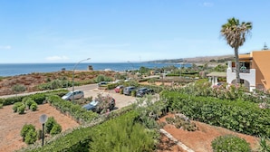 Ein Küstenwohngebiet mit geparkten Autos, üppigem Grün und Blick auf das Meer.