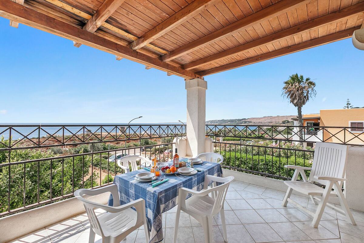 A balcony with a table set for two, overlooking a coastal landscape.