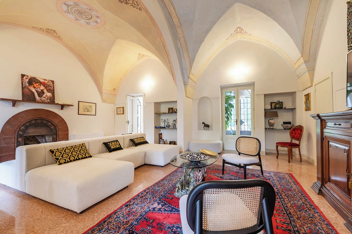 A spacious living room with a large white sofa, a glass coffee table, and a red patterned rug.