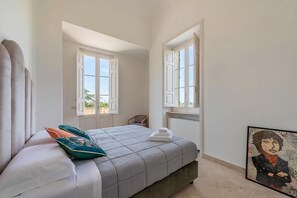 Une chambre à coucher avec un lit, deux fenêtres, une chaise et un tableau accroché au mur.