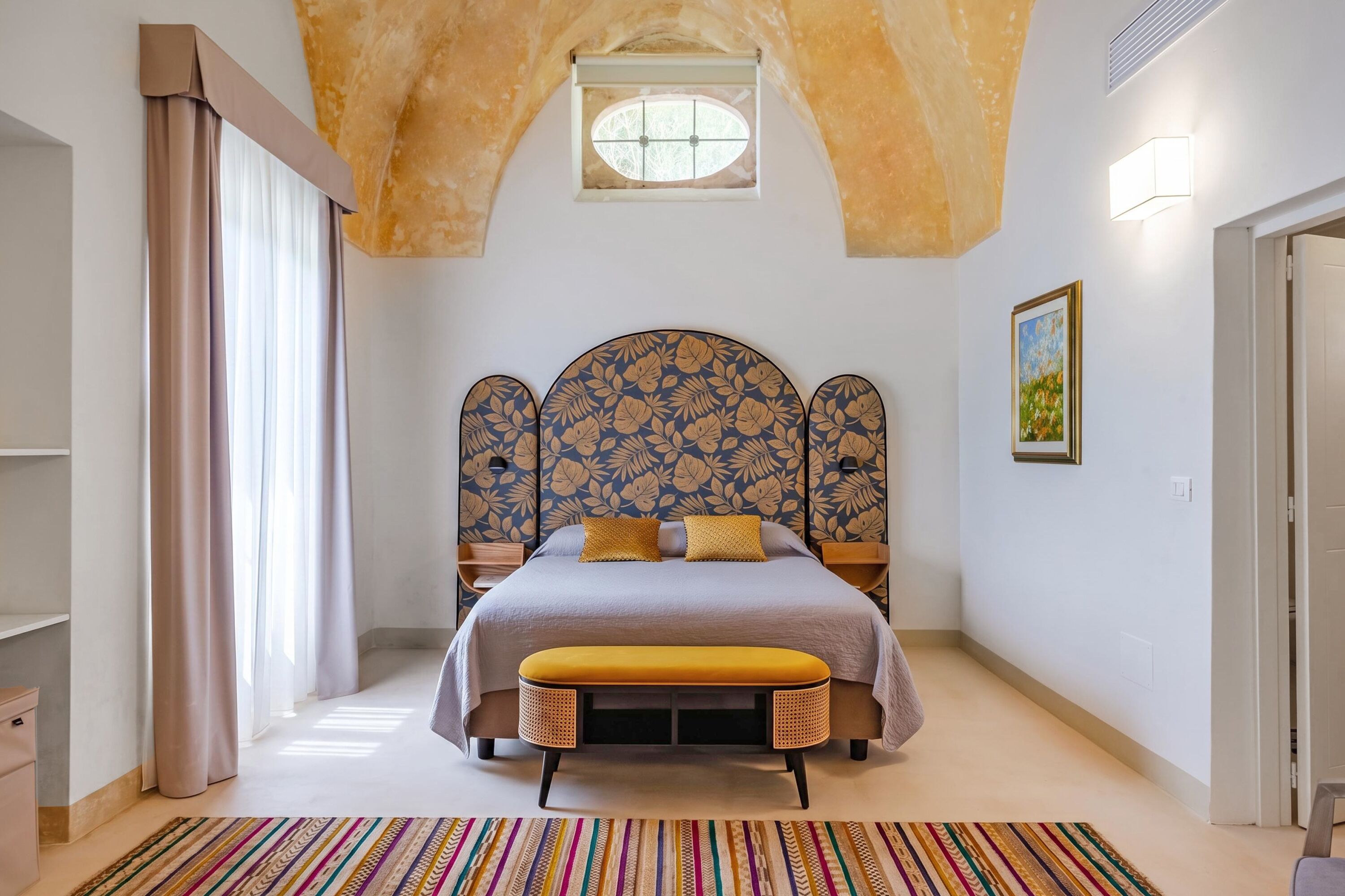 A bedroom with a bed, a bench, a window, and a painting on the wall.