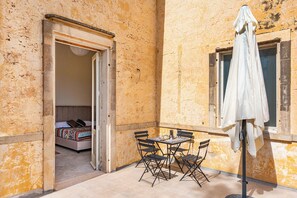 A small outdoor patio with a table and chairs, a white umbrella, and a bed visible through an open doorway. - Vallone Apartments (Galatina)