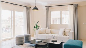 A modern living room with a white sofa, a black coffee table, and a teal ottoman. There is a potted plant and a hanging light fixture. - VIDA in Yasmeen - V201, VIDA Garden View Apartment (New Cairo City)