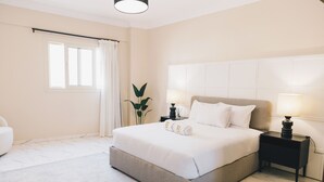A modern hotel room with a large bed, a bedside table with a lamp, a window with curtains, and a potted plant. - VIDA in Yasmeen - V201, VIDA Garden View Apartment (New Cairo City)