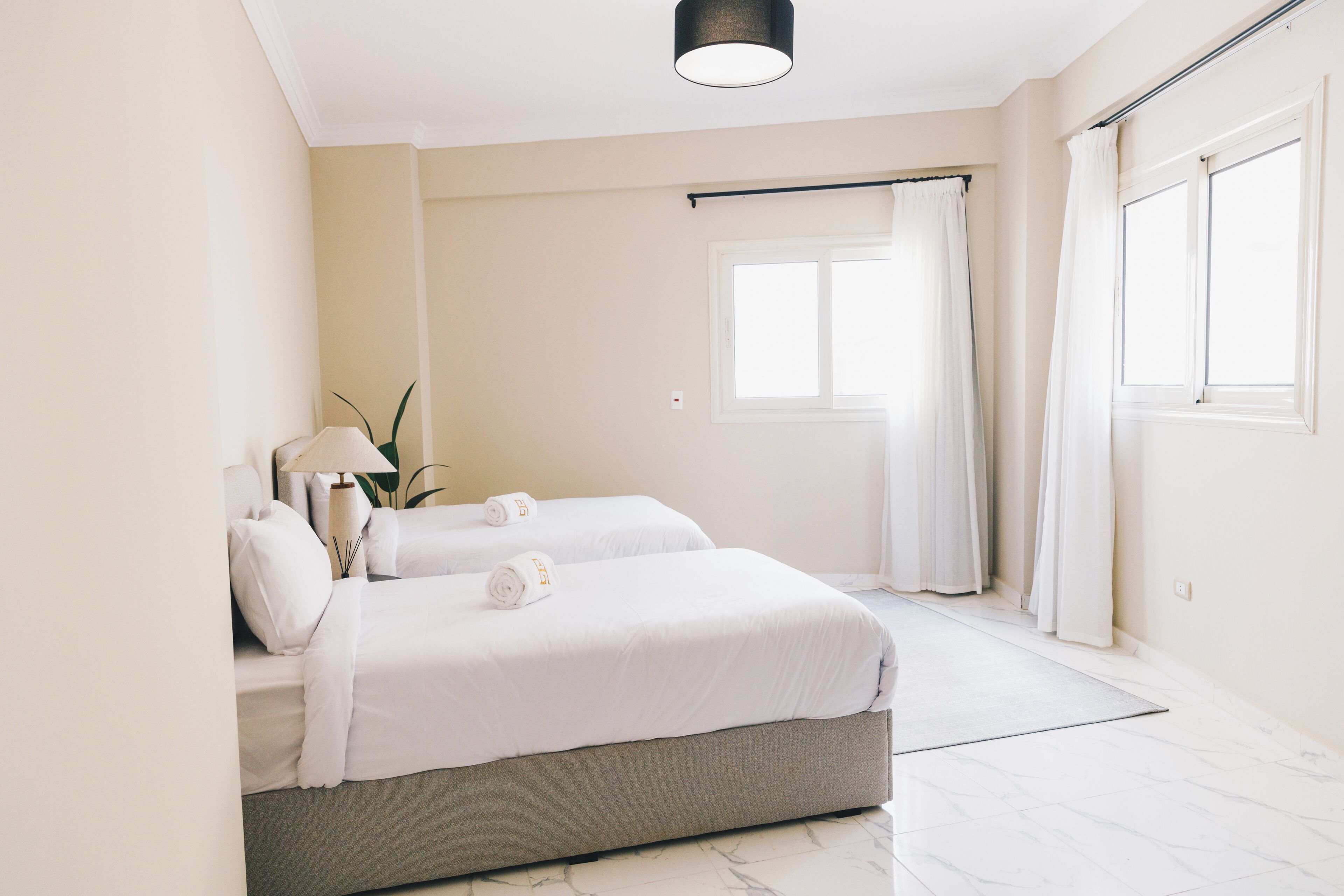 Una habitación de hotel moderna con dos camas, un ventanal con cortinas, una lámpara de techo y suelo de mármol.