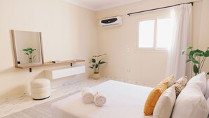 Habitación de hotel moderna con una cama grande, una mesita de noche, un espejo, una planta en maceta y un equipo de aire acondicionado.