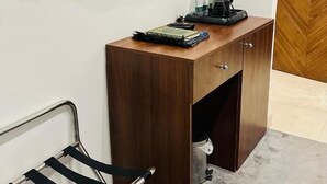 Une petite pièce comprenant un bureau en bois, un miroir, une chaise et une machine à café.