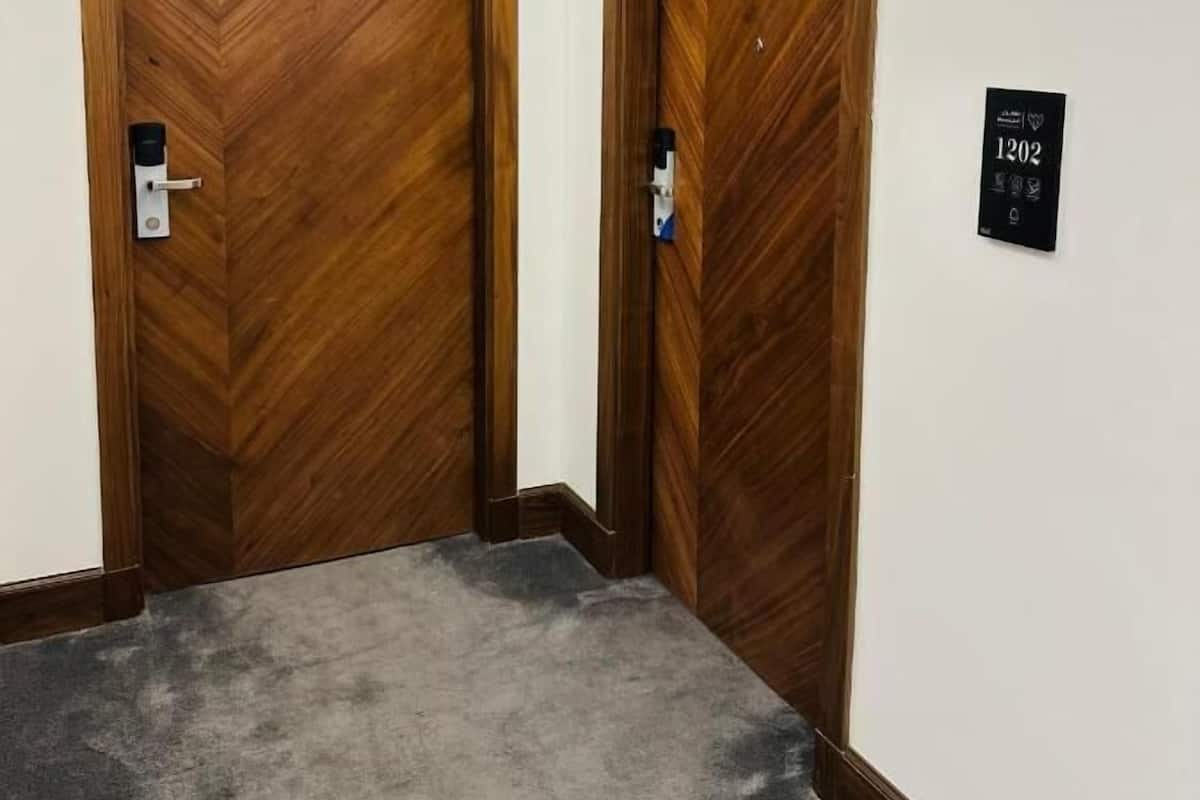 Un pasillo con dos puertas de madera, piso alfombrado y un letrero en la pared con el número 1202.