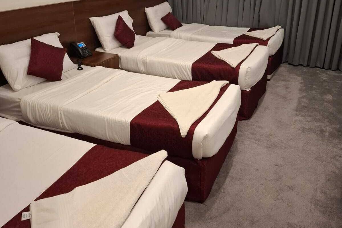 Habitación de hotel con cuatro camas dispuestas en fila, cada una con ropa de cama blanca y roja, cabecero de madera y un teléfono en la mesita de noche.
